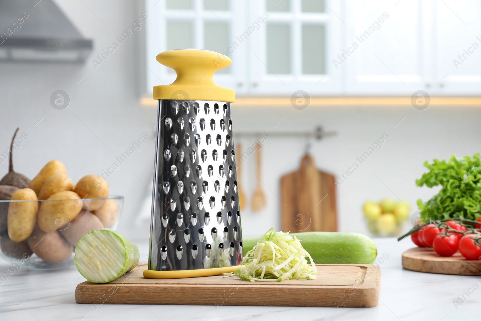 Photo of Grater and fresh zucchinis on white table in kitchen. Space for text