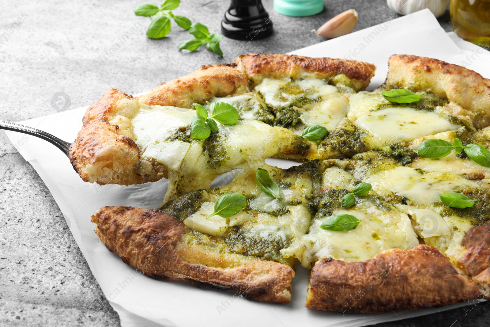 Photo of Taking slice of delicious pizza with pesto, cheese and basil on grey table, closeup