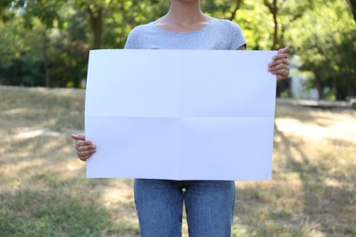 Woman holding blank poster outdoors, closeup. Mockup for design	