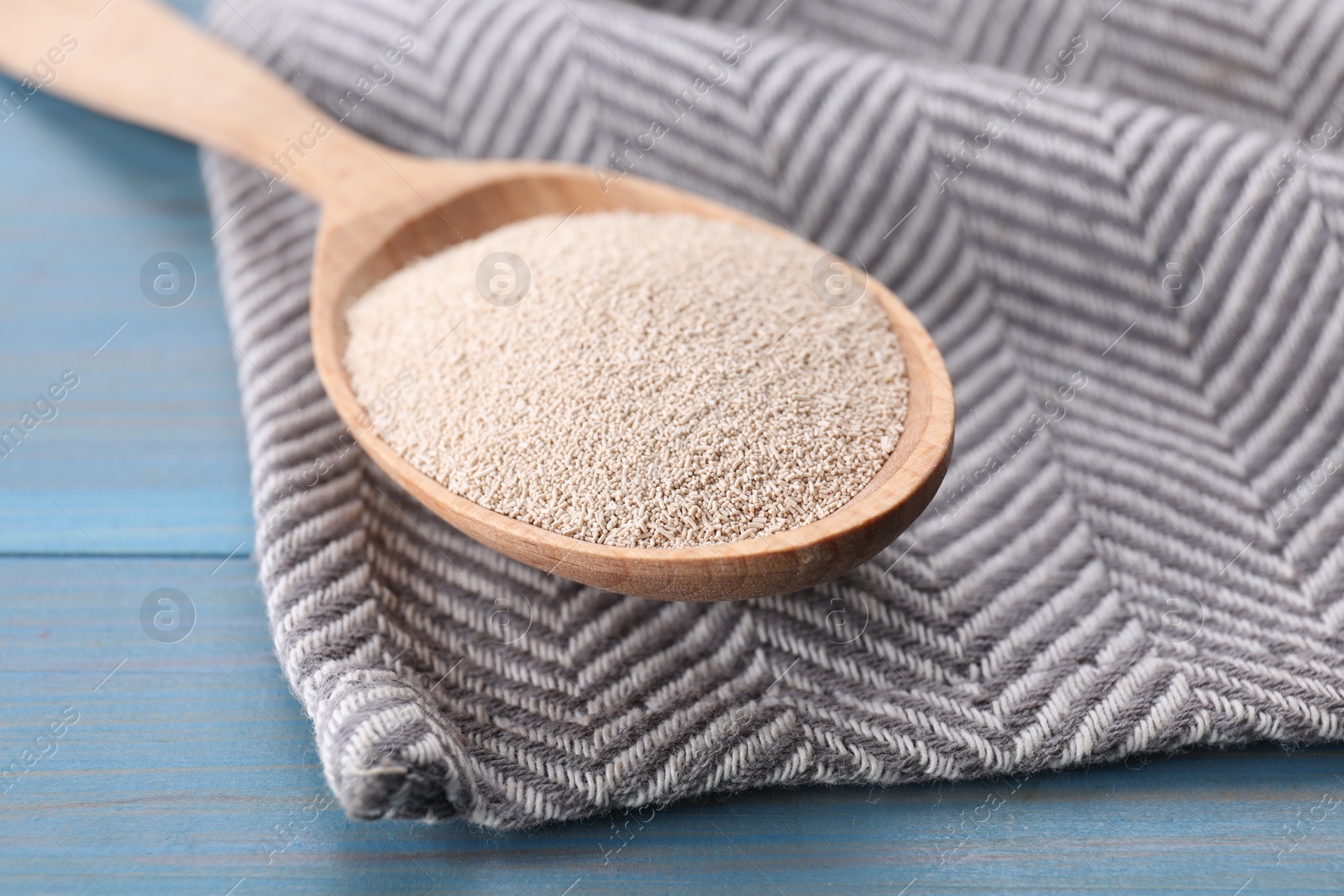 Photo of Spoon with active dry yeast on light blue wooden table, closeup
