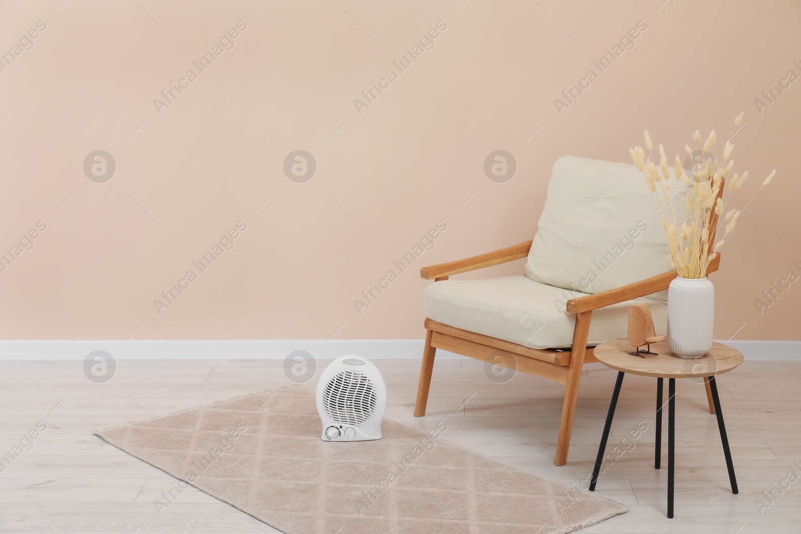 Photo of Compact electric fan heater near armchair indoors, space for text