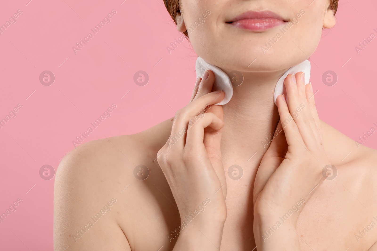 Photo of Woman with freckles wiping neck on pink background, closeup