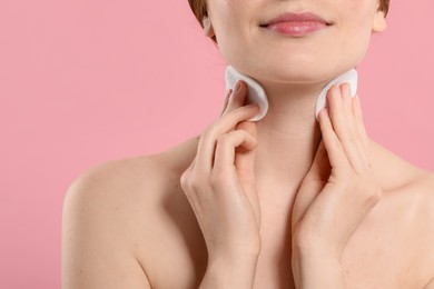 Photo of Woman with freckles wiping neck on pink background, closeup