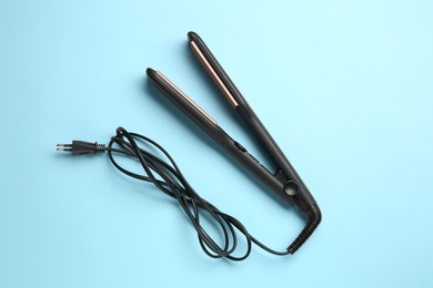 Modern flat hair iron on light blue background, top view