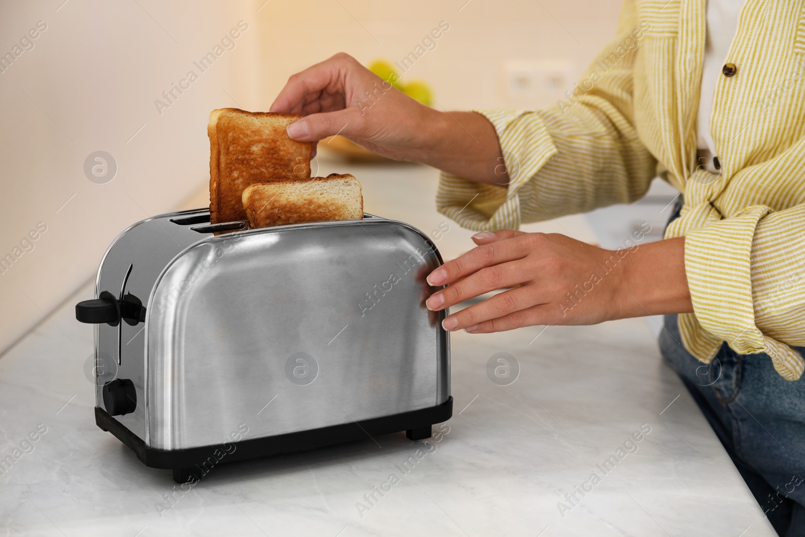 Photo of Woman taking slice of bread from toaster in kitchen, closeup