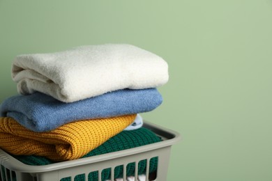 Photo of Plastic laundry basket with clean clothes near light green wall, closeup. Space for text