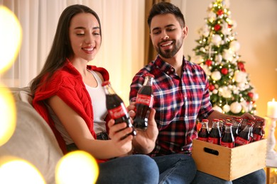 Photo of MYKOLAIV, UKRAINE - JANUARY 27, 2021: Young couple holding bottles of Coca-Cola in room decorated for Christmas