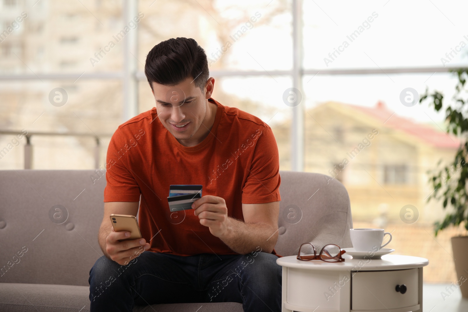 Photo of Man using smartphone and credit card for online payment on sofa at home