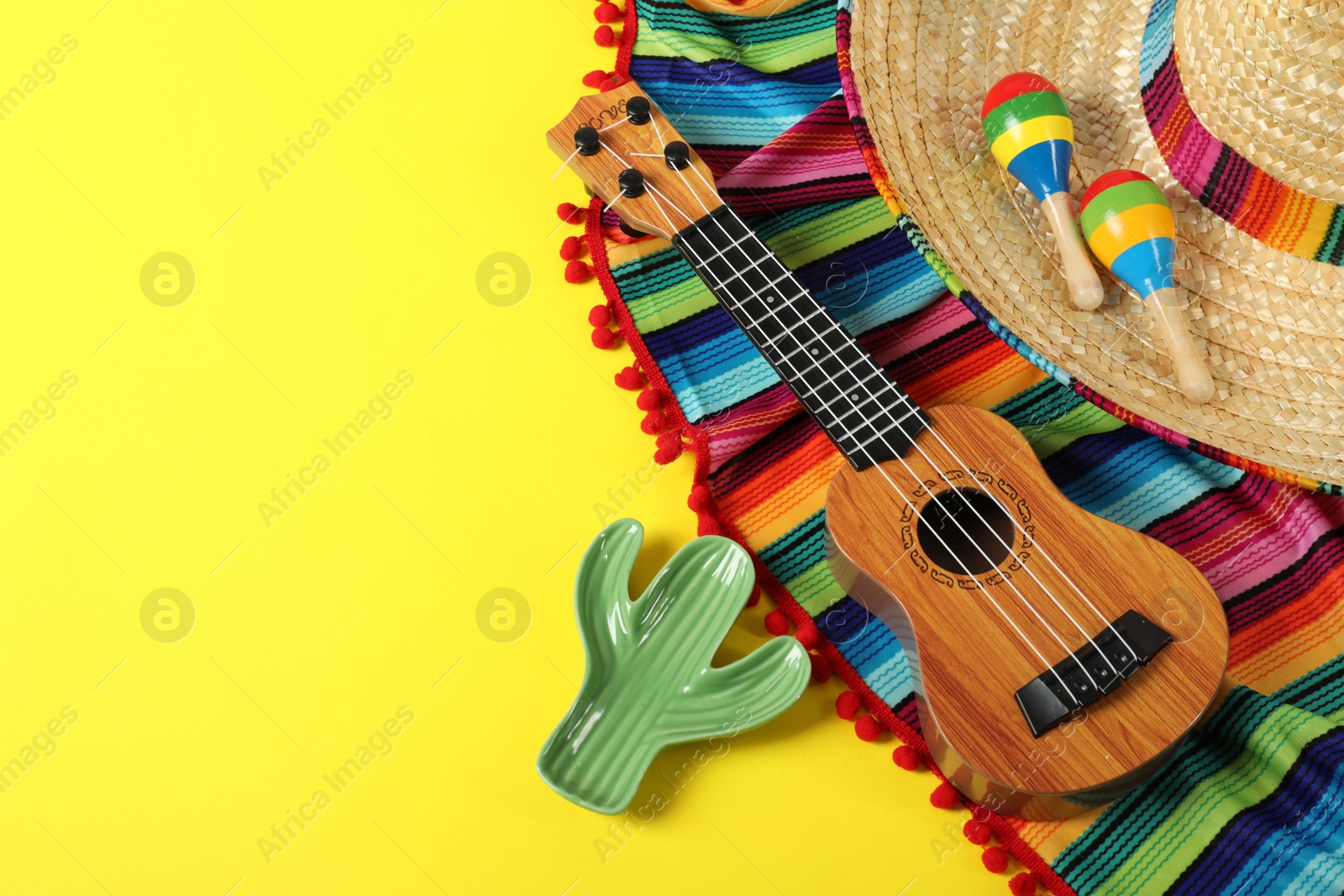 Photo of Composition with Mexican sombrero hat, ukulele and maracas on yellow table, above view. Space for text