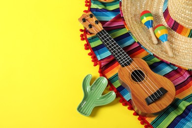 Photo of Composition with Mexican sombrero hat, ukulele and maracas on yellow table, above view. Space for text