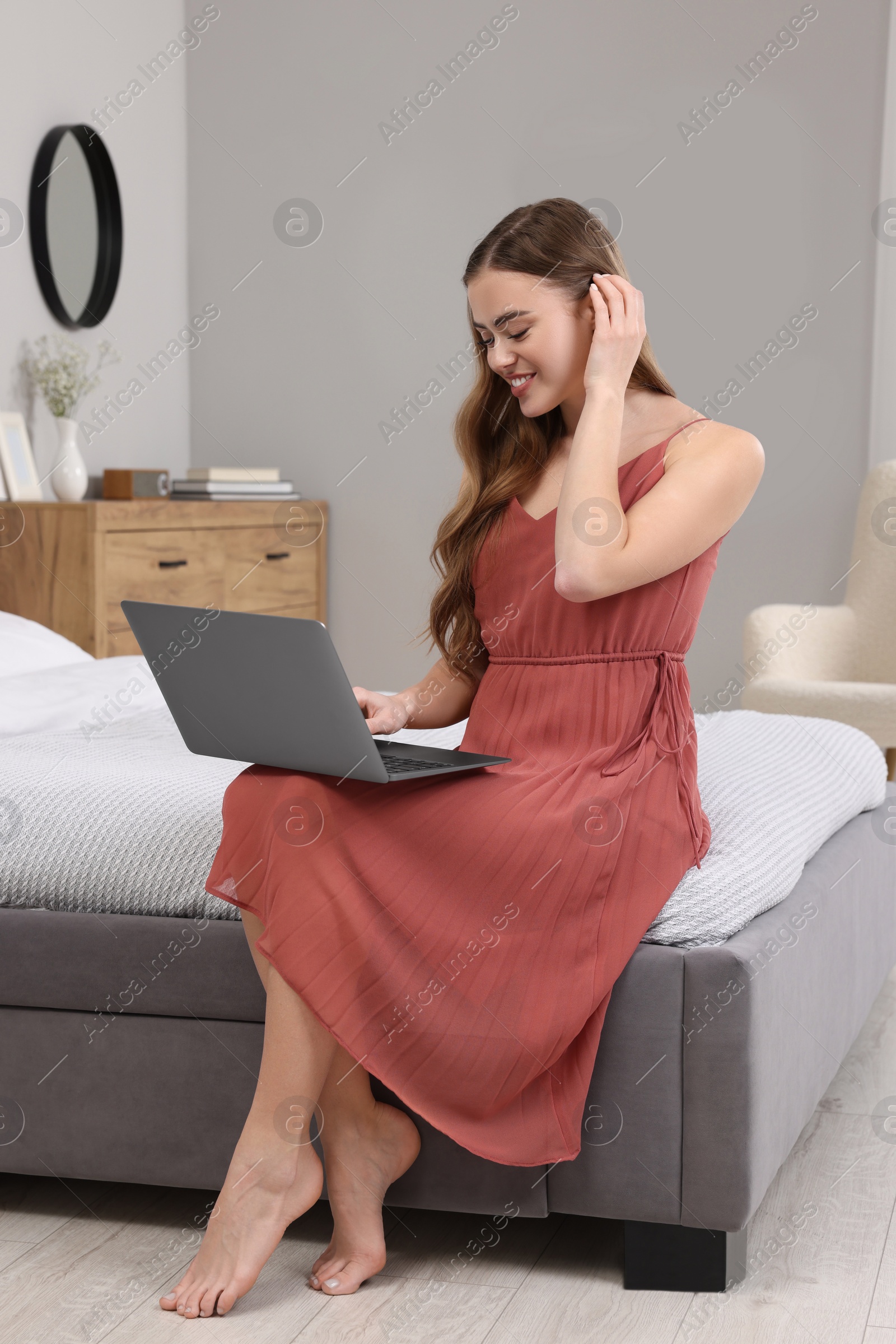 Photo of Happy woman with laptop on bed in bedroom