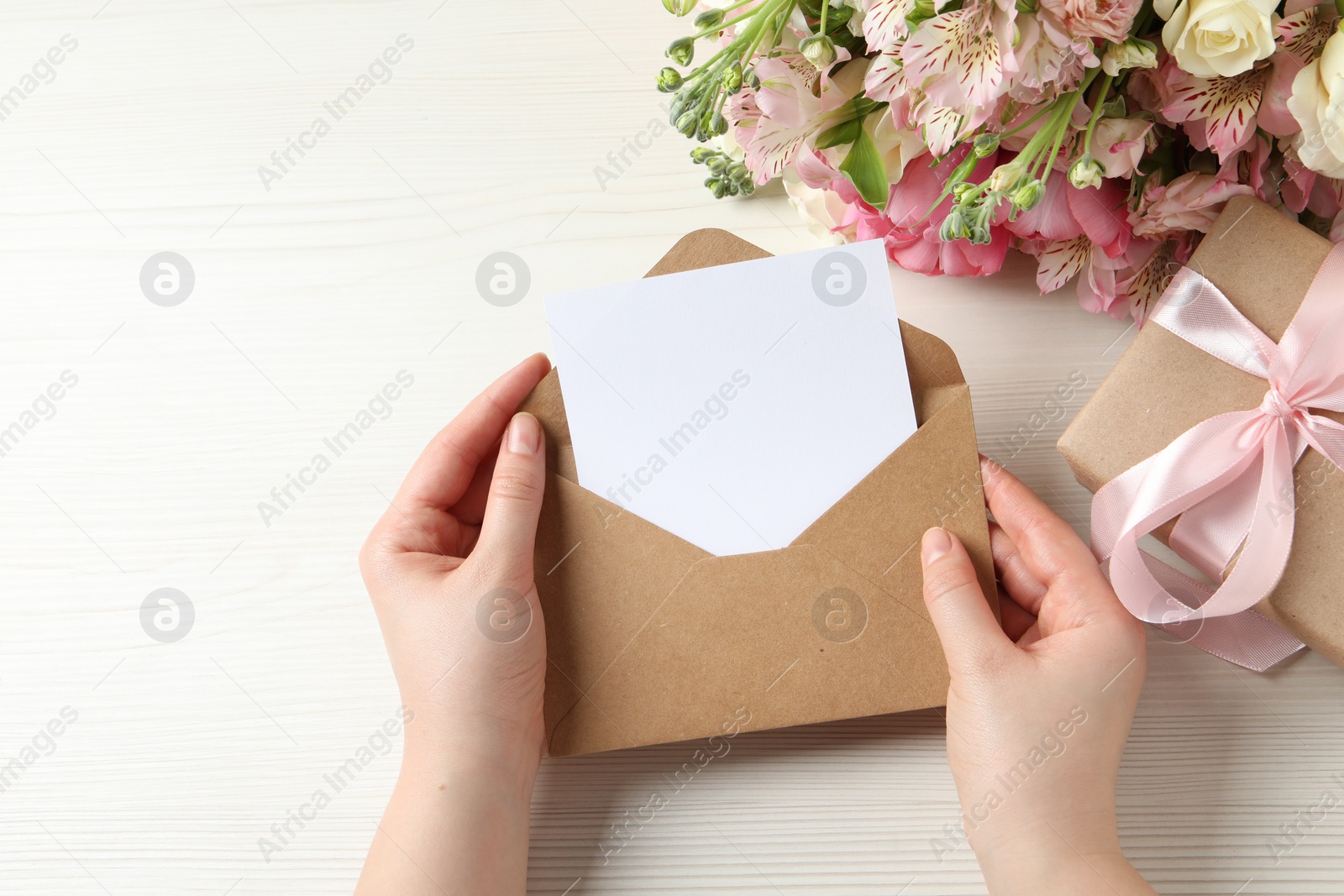 Photo of Happy Mother's Day. Woman holding envelope with blank card at white wooden table, top view