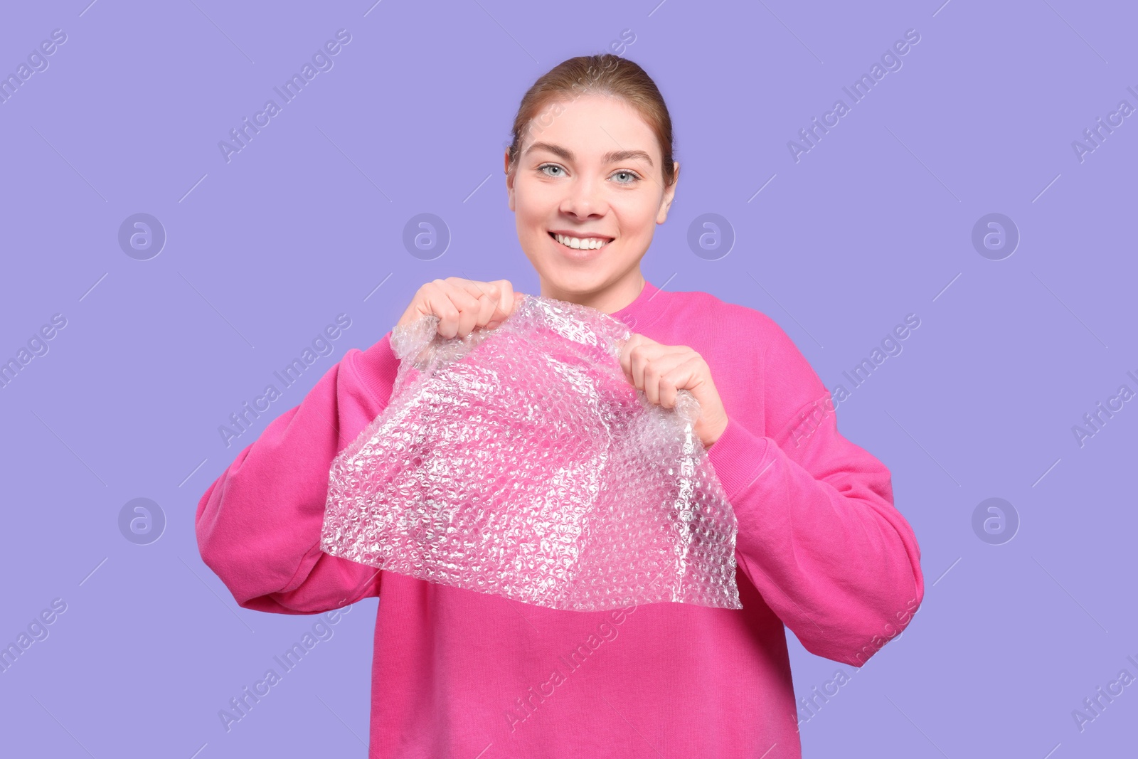 Photo of Woman popping bubble wrap on purple background. Stress relief