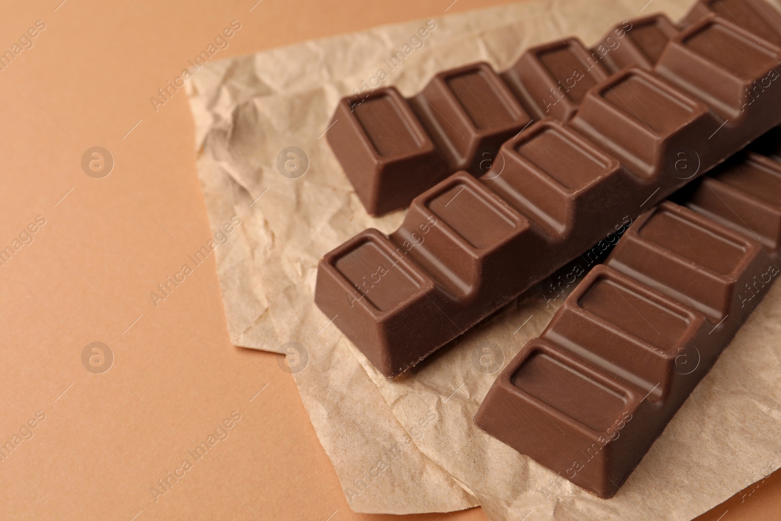 Photo of Parchment with delicious chocolate bars on light brown background, closeup