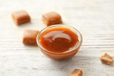 Delicious caramel candies and sauce on wooden background