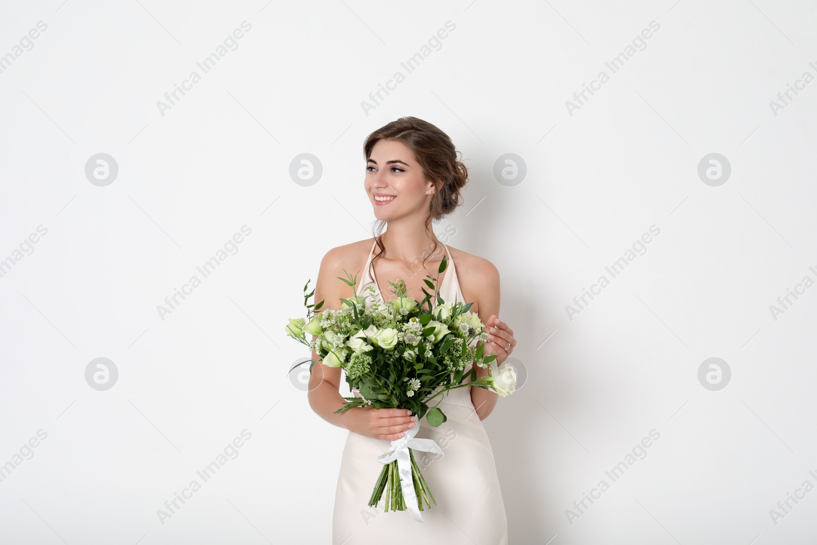 Photo of Young bride wearing wedding dress with beautiful bouquet on light background