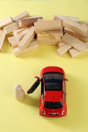 Photo of Overcoming barries for development and success. Wooden human figure near red toy car in front of blocks on yellow background