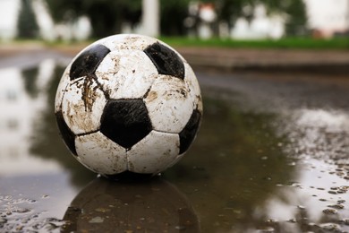 Dirty soccer ball near puddle outdoors, space for text
