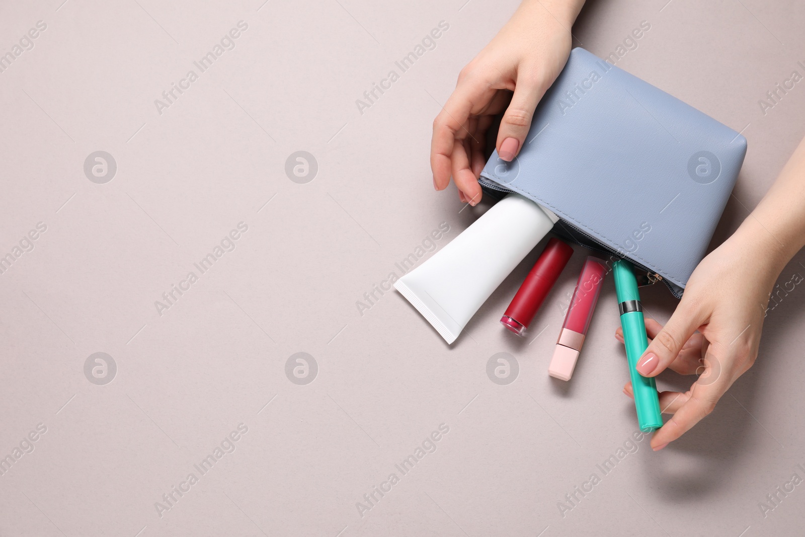 Photo of Woman with cosmetic bag and different makeup products on beige background, top view. Space for text