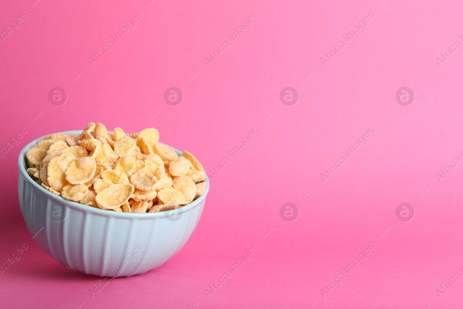 Photo of Bowl of tasty crispy corn flakes on pink background, space for text