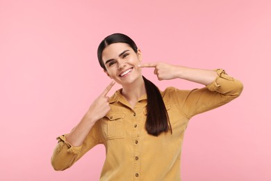 Photo of Woman pointing at her clean teeth and smiling on pink background