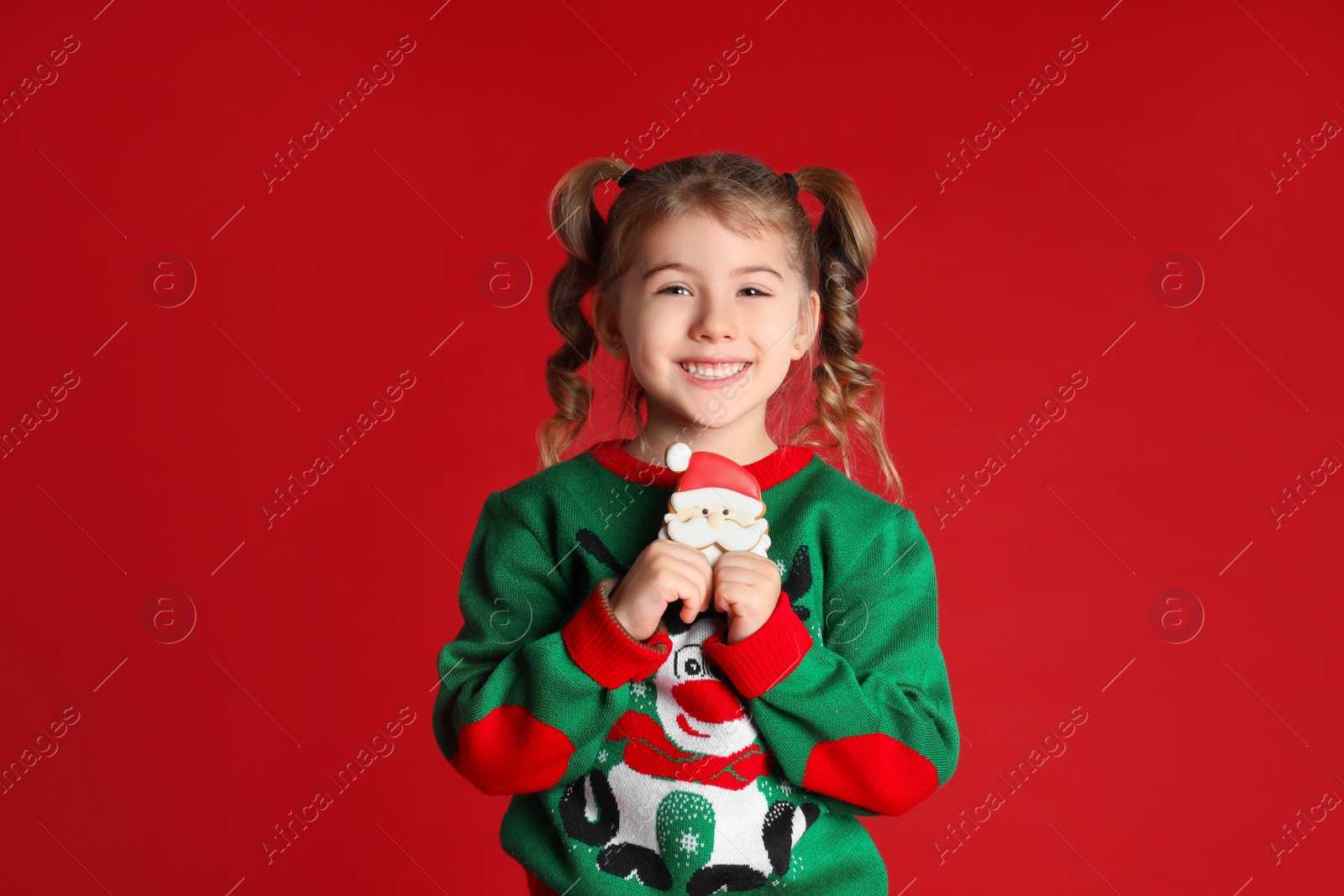 Photo of Cute little girl with Christmas gingerbread cookie on red background