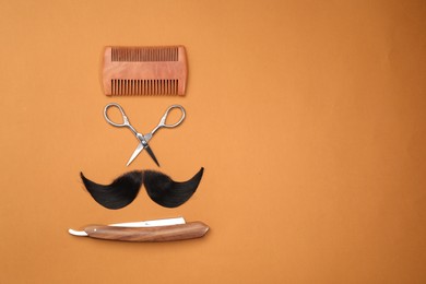 Photo of Artificial moustache and barber tools on orange background, flat lay. Space for text