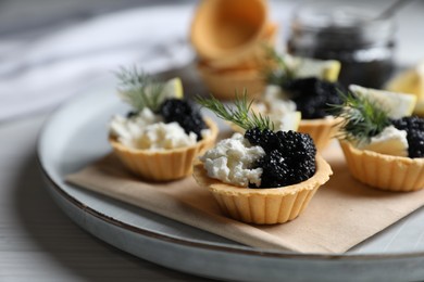 Photo of Delicious tartlets with black caviar, cream cheese and lemon served on light table, closeup