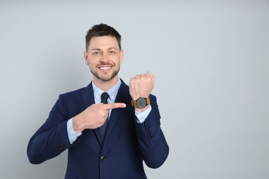 Happy businessman pointing on wristwatch against grey background, space for text. Time management