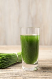 Wheat grass drink in shot glass and fresh green sprouts on wooden table, closeup