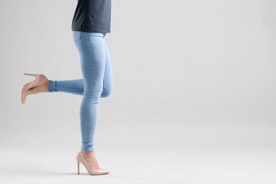 Photo of Woman wearing stylish jeans and high heels shoes on light gray background, closeup. Space for text