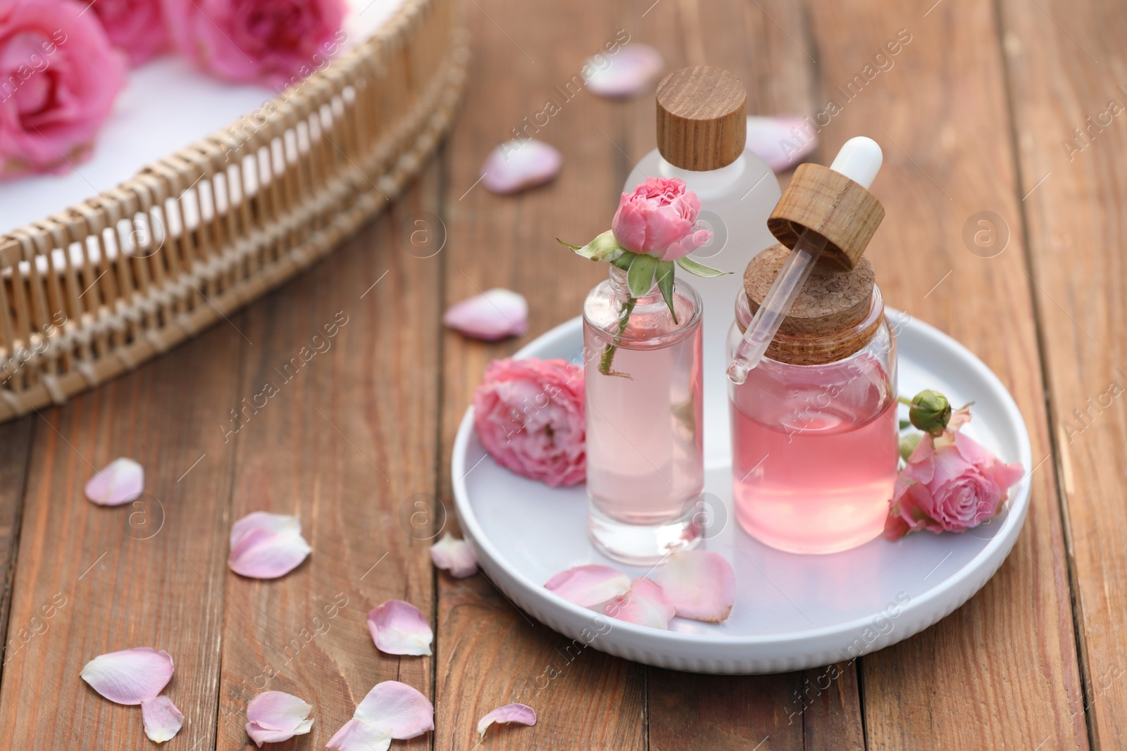 Photo of Bottles of rose essential oil and flowers on wooden table, space for text