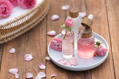 Bottles of rose essential oil and flowers on wooden table, space for text