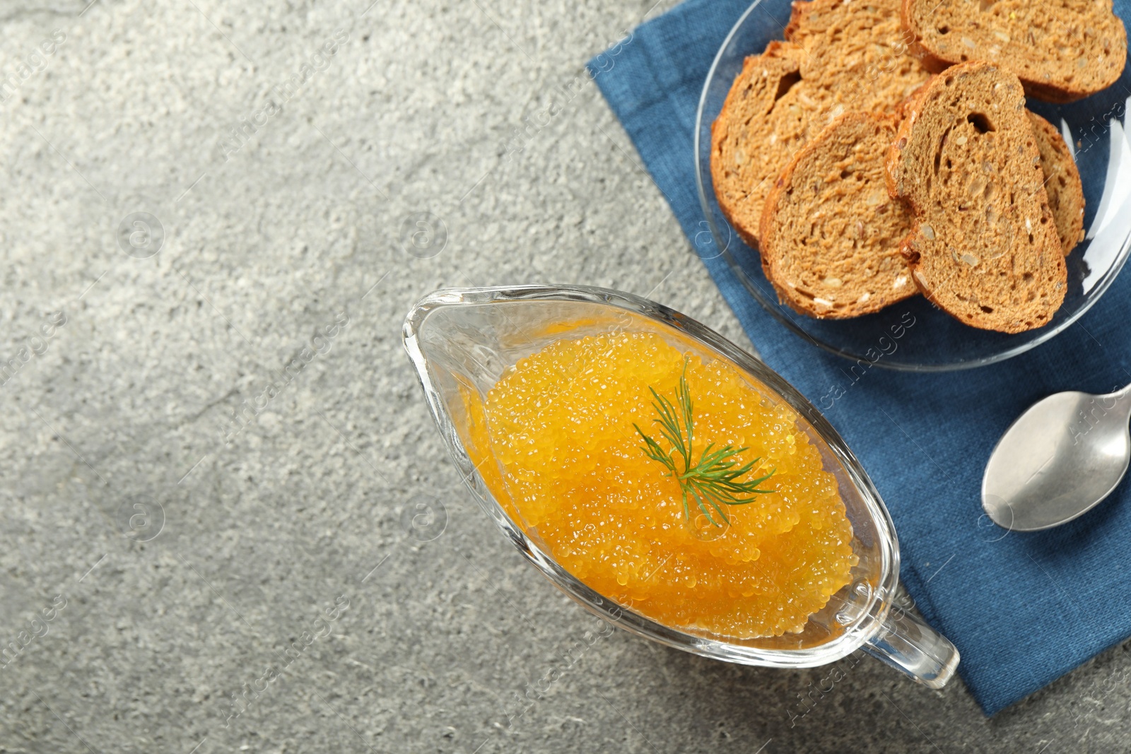 Photo of Fresh pike caviar in gravy boat, bread and spoon on grey table, top view. Space for text