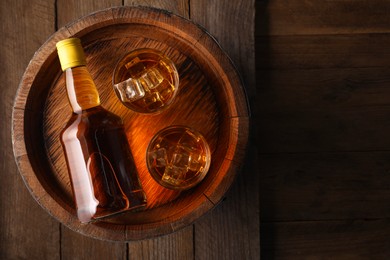 Photo of Whiskey with ice cubes in glasses, bottle and barrel on wooden table, top view. Space for text