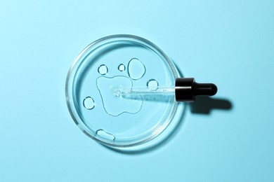 Photo of Petri dish with pipette on light blue background, top view
