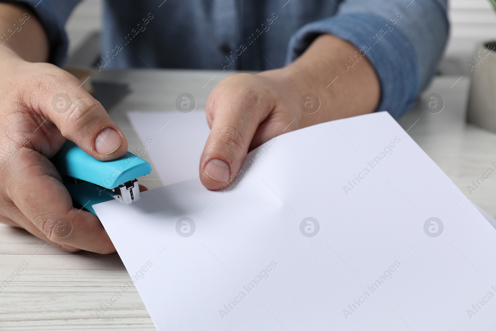 Photo of Man with papers using stapler at white wooden table, closeup