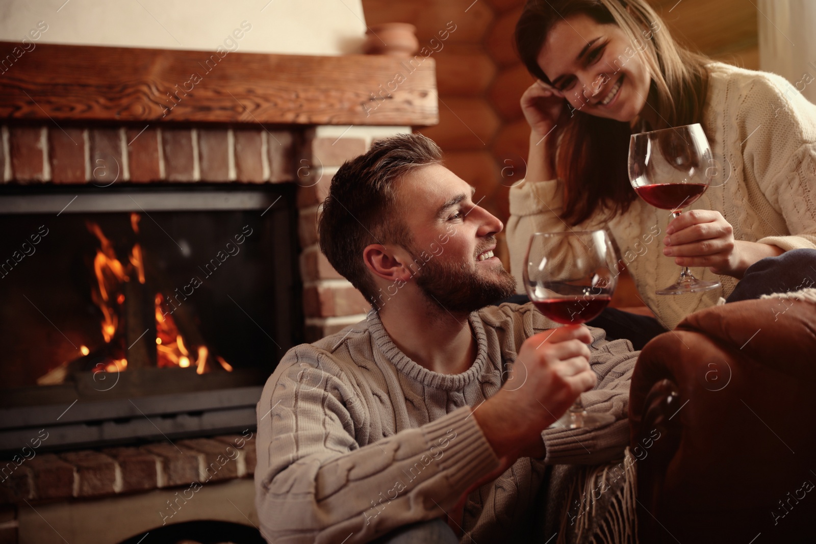 Photo of Lovely couple with glasses of wine near fireplace indoors. Winter vacation