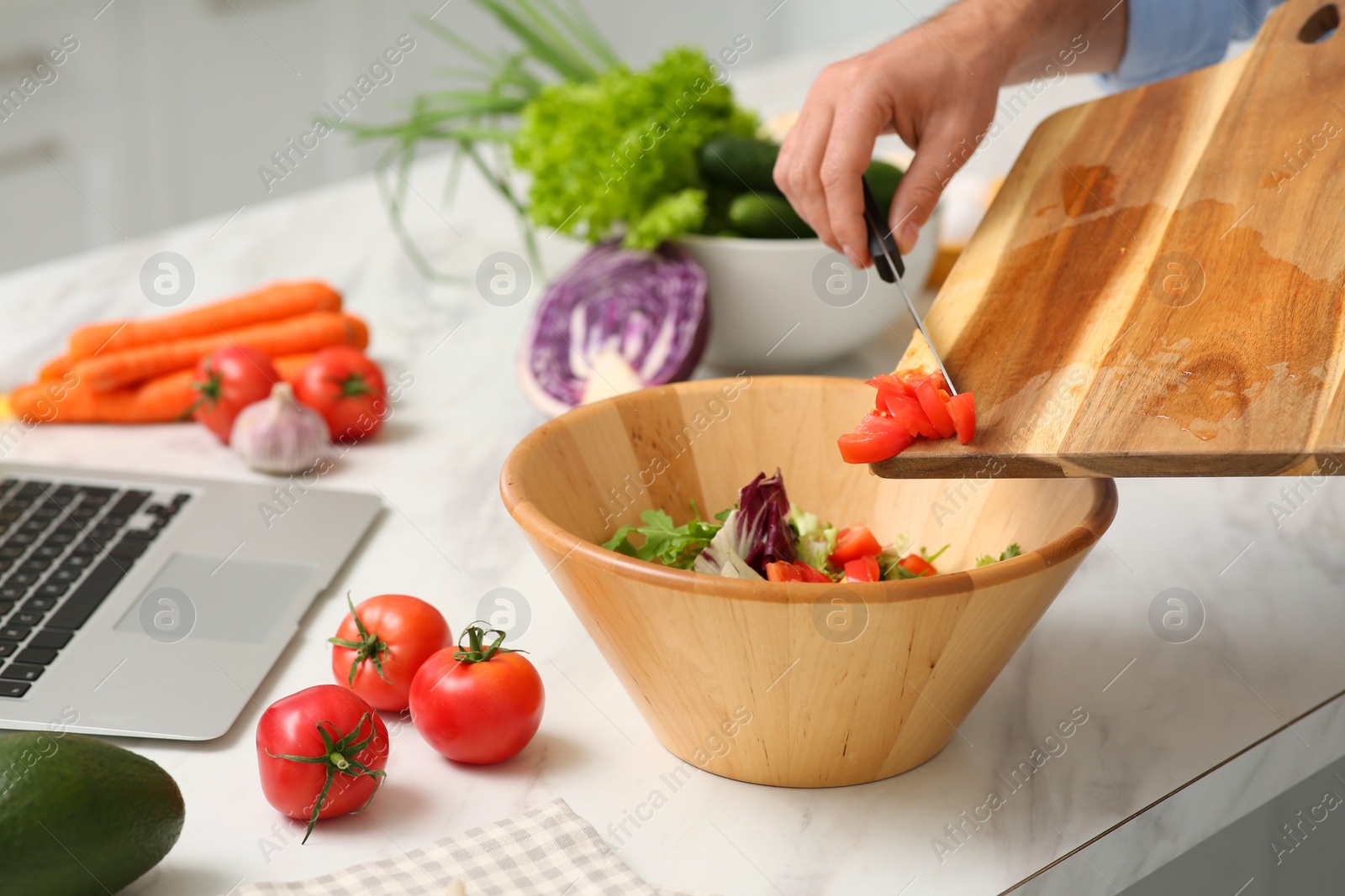 Photo of Man making dinner while watching online cooking course via laptop at table, closeup