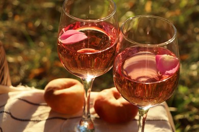 Photo of Glassesdelicious rose wine with petals and peaches on white picnic blanket outside, closeup