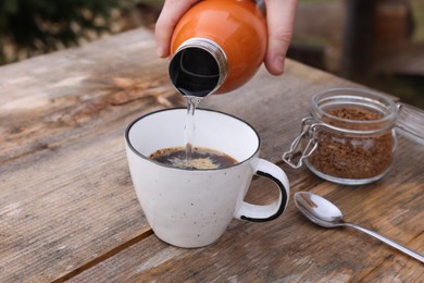 Photo of Woman pouring hot water into cup with instant coffee at wooden table outdoors, closeup