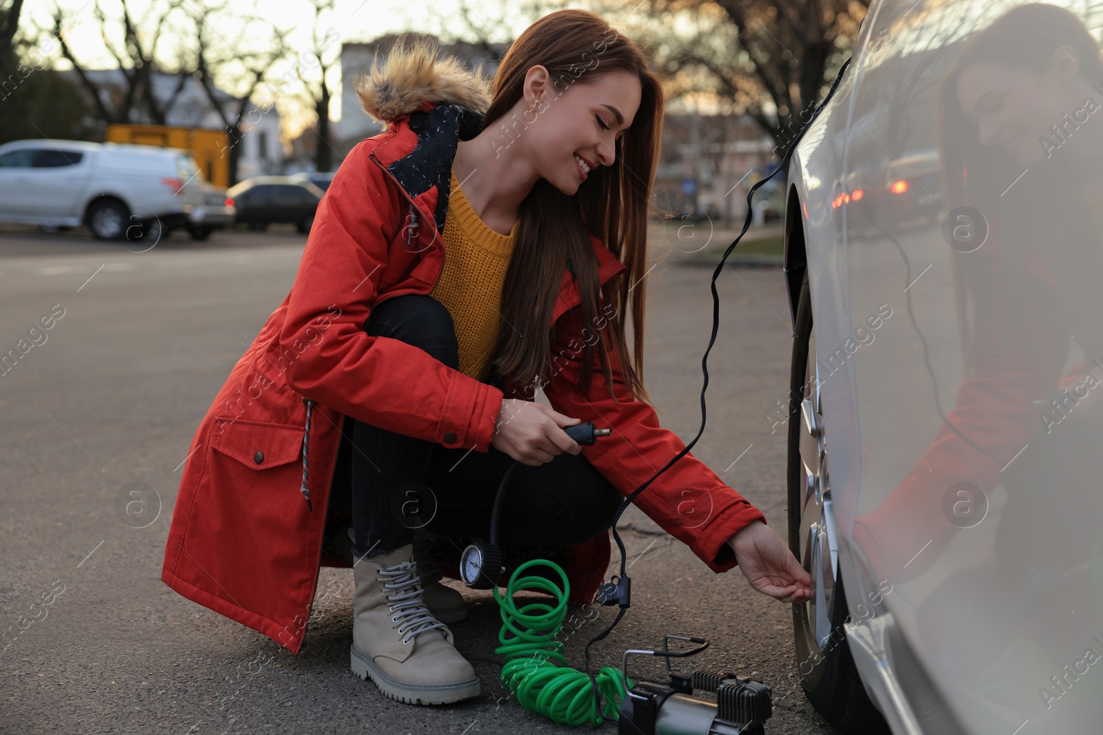 Photo of Young woman inflating car tire with air compressor on street