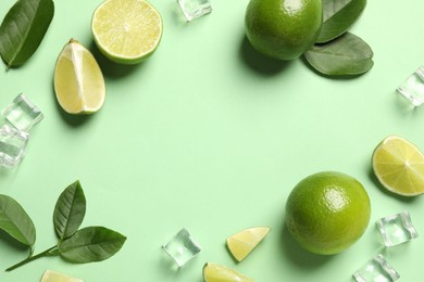 Photo of Frame made of ripe limes with leaves and ice cubes on light green background, flat lay