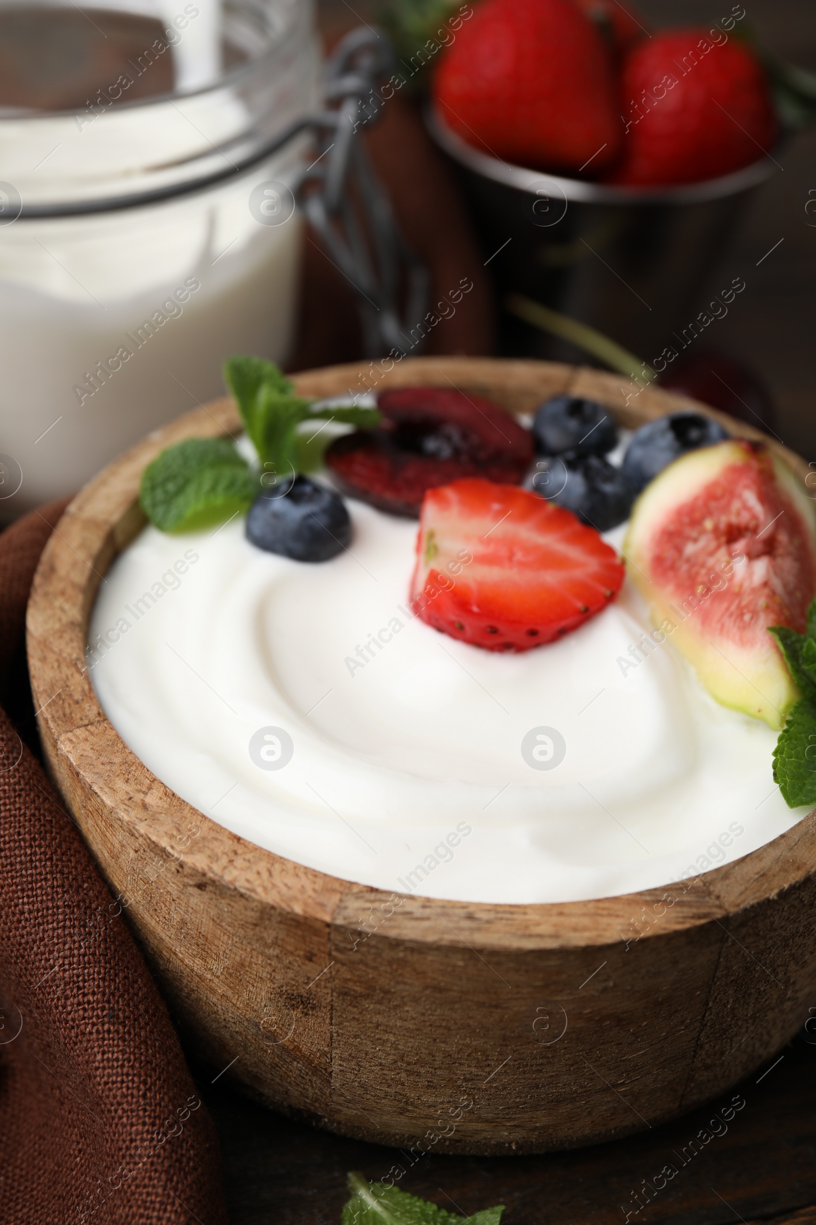 Photo of Bowl with yogurt, berries, fruits and mint on wooden table, closeup