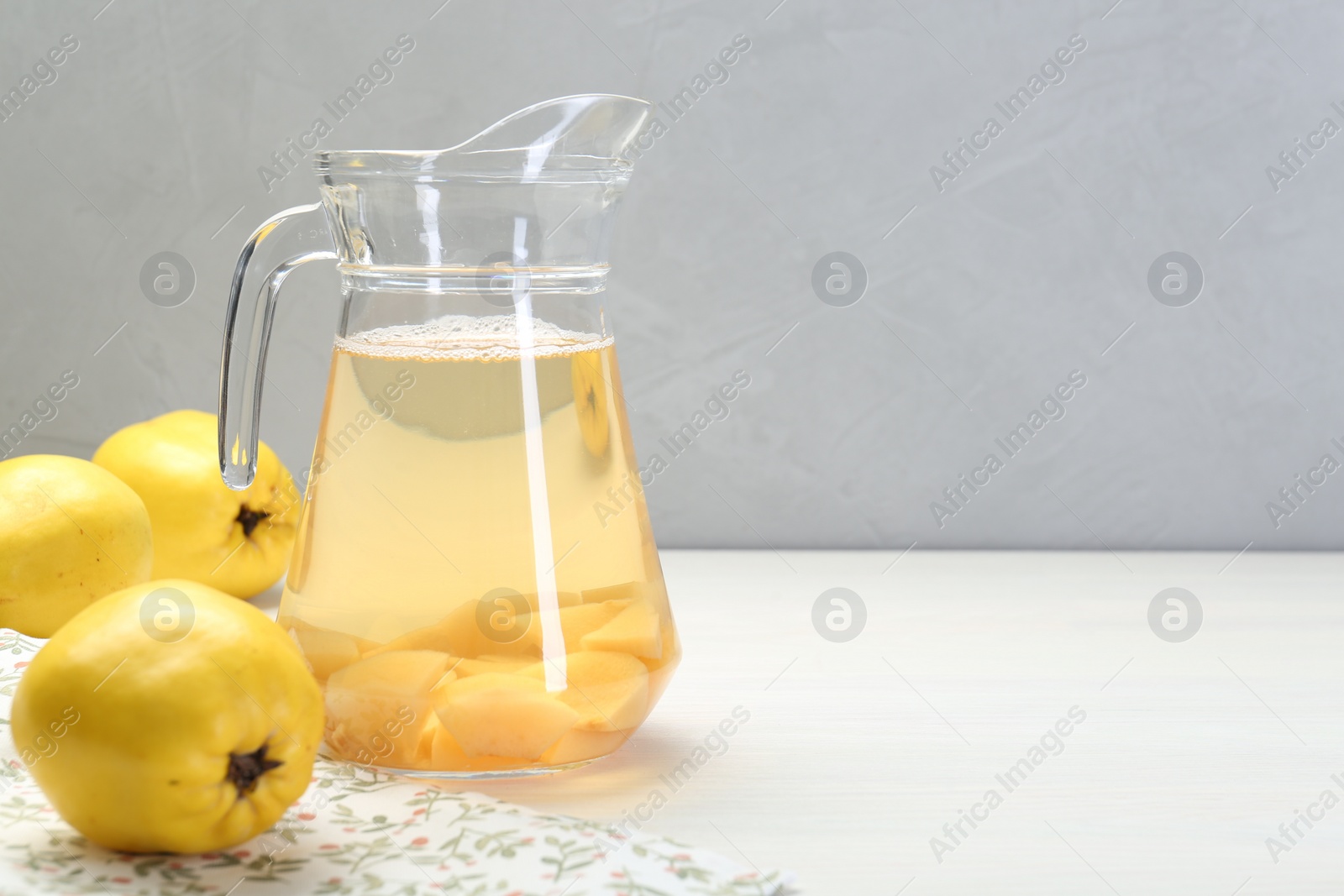 Photo of Delicious quince drink in glass jug and fresh fruits on white wooden table, space for text