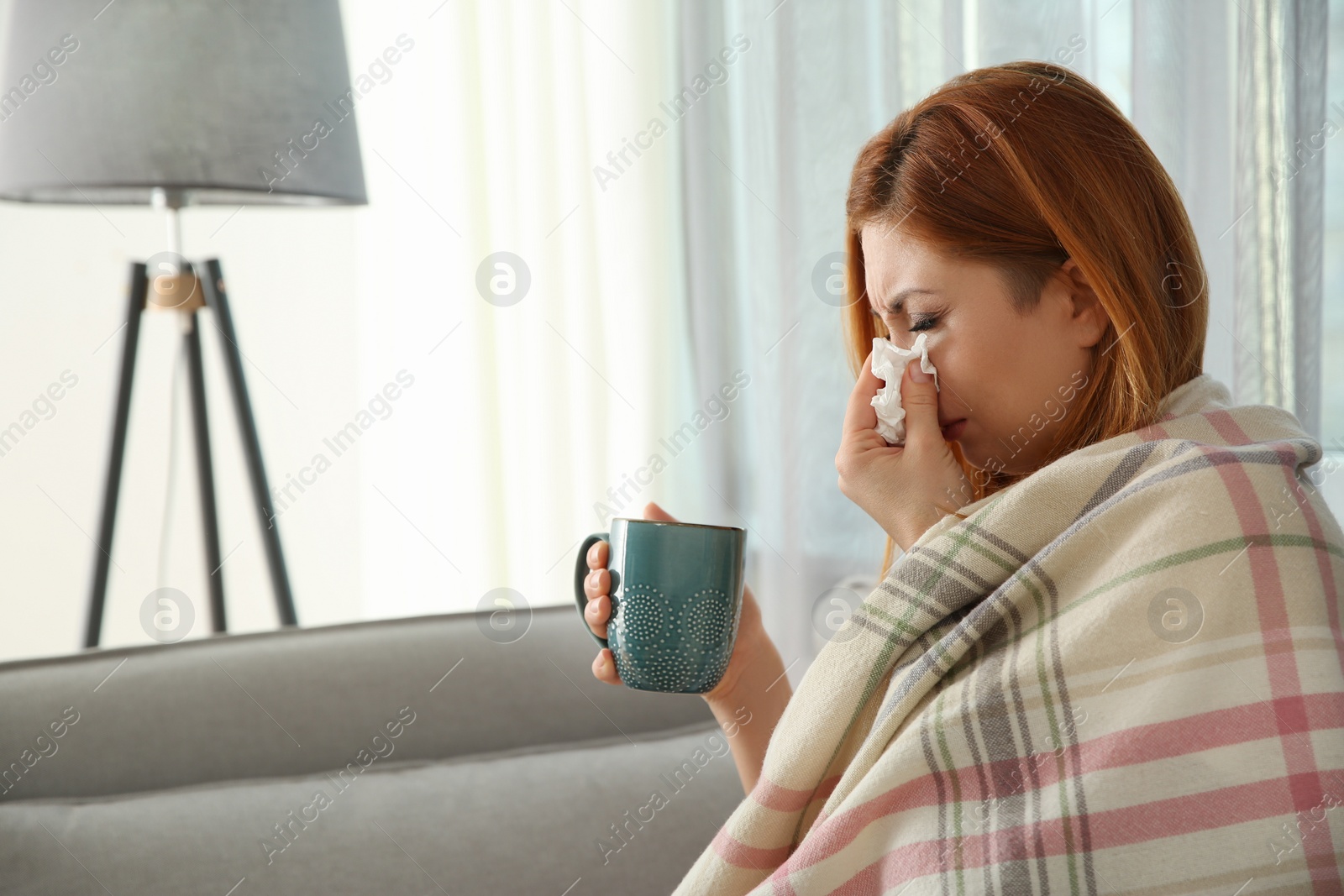 Photo of Sick woman wrapped in plaid with cup of hot drink at home. Influenza virus