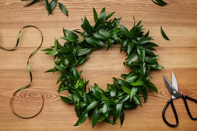 Photo of Beautiful handmade mistletoe wreath and florist supplies on wooden table, flat lay. Traditional Christmas decor