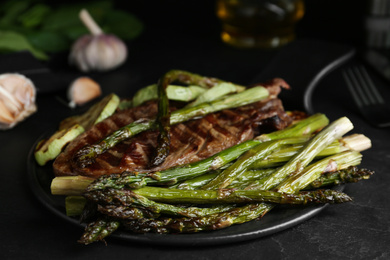 Tasty asparagus with grilled meat on black table