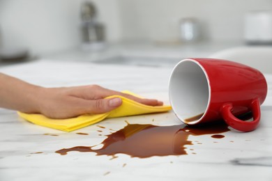 Photo of Woman cleaning spilled coffee on white marble table in kitchen, closeup