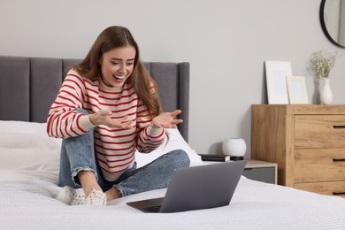 Surprised woman with laptop on bed in bedroom